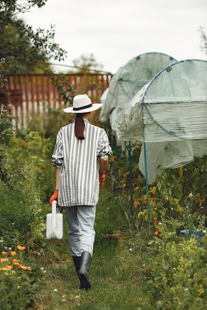 Giardinaggio in estate. Donna che innaffia i fiori con un annaffiatoio. Ragazza che indossa un cappello.