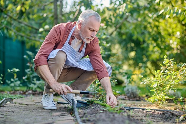 Giardinaggio. Uomo di mezza età che lavora in un giardino con inventario gtareden