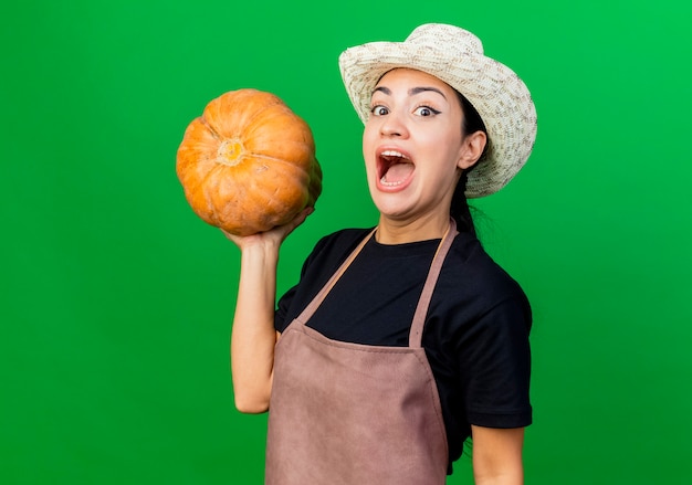 Giardiniere della giovane bella donna in grembiule e cappello che tengono zucca felice ed emozionato