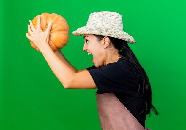 Giardiniere della giovane bella donna in grembiule e cappello che tiene la zucca che grida