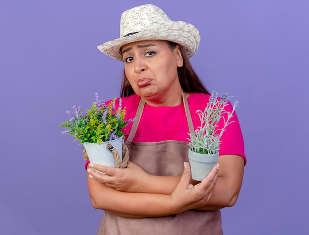 Giardiniere donna di mezza età in grembiule e cappello con piante in vaso