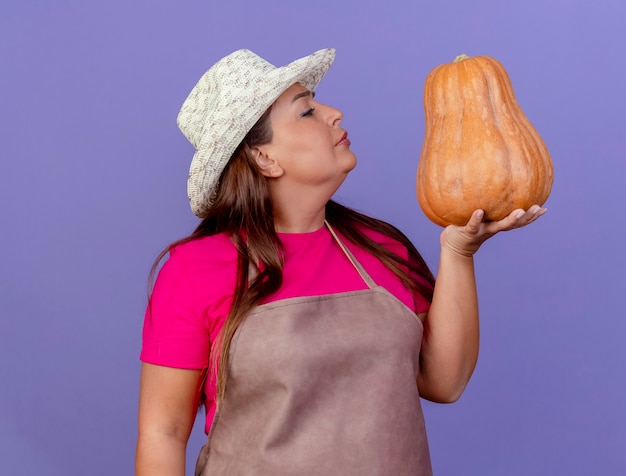 Giardiniere donna di mezza età in grembiule e cappello tenendo la zucca guardando incuriosito