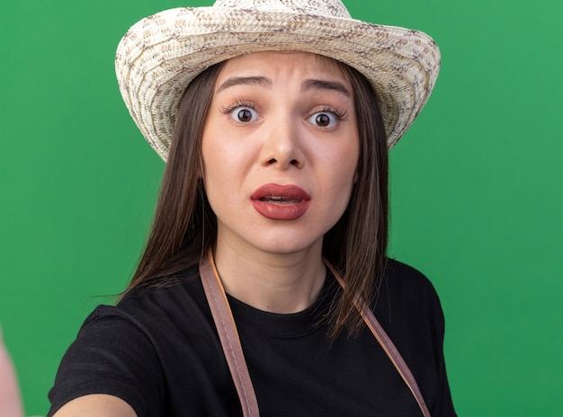 Giardiniere femminile abbastanza caucasico ansioso che porta il cappello di giardinaggio che guarda l'obbiettivo sul verde