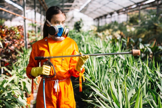 Giardiniere femminile con lo spruzzatore che sta nella serra