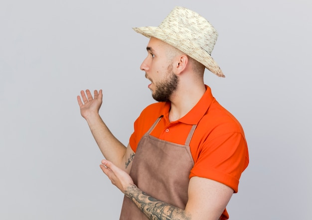Giardiniere maschio scioccato indossando punti di giardinaggio cappello dietro con due mani che guardano a lato