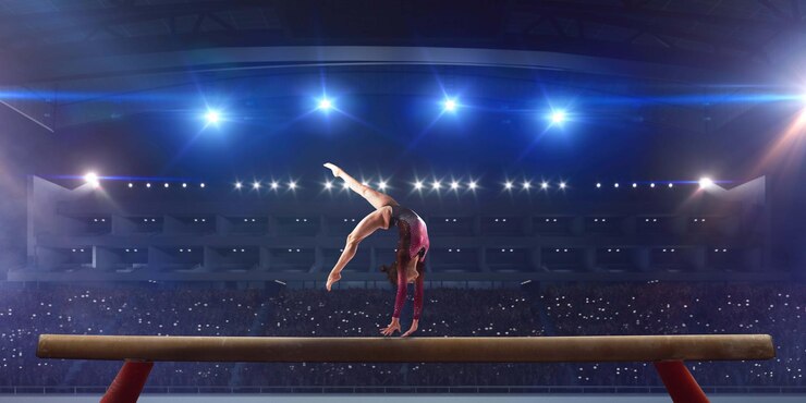 Ginnasta che fa un trucco complicato sulla trave di bilanciamento della ginnastica in un'arena professionale