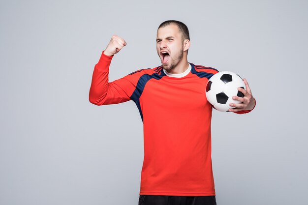 Giocatore di calcio emozionante in maglietta rossa che tiene un concetto di vittoria di calcio isolato su bianco