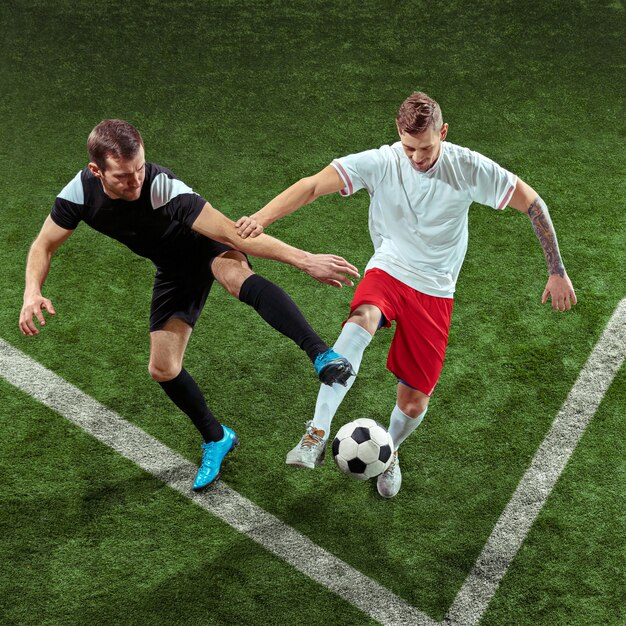 Giocatore di football americano che affronta per palla sopra il muro di erba verde. Giocatori di calcio maschi professionisti in movimento allo stadio. Montare uomini che saltano in azione, saltare, muoversi durante il gioco.