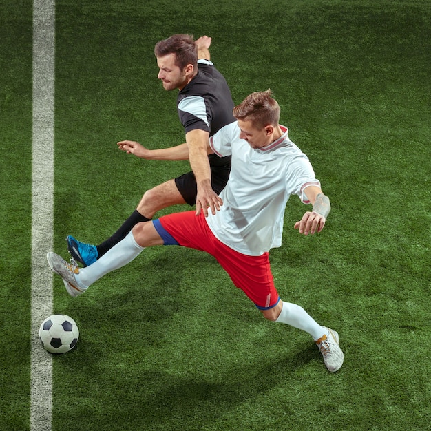 Giocatore di football americano che affronta per palla sopra il muro di erba verde. Giocatori di calcio maschi professionisti in movimento allo stadio. Montare uomini che saltano in azione, saltare, muoversi durante il gioco.