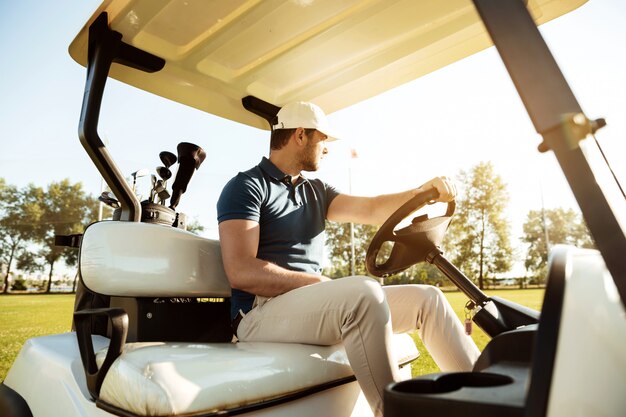 Giocatore di golf maschio che guida un carrello con la borsa dei club di golf