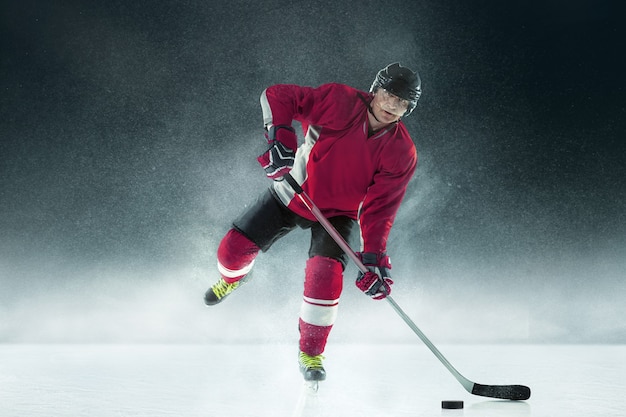 Giocatore di hockey maschio con il bastone sul campo da ghiaccio e muro scuro