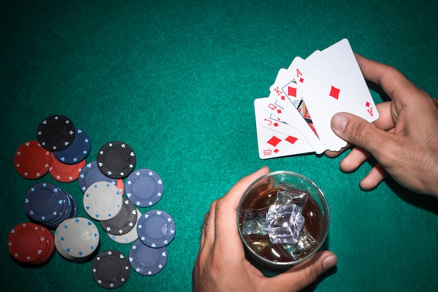 Giocatore di poker con bicchiere di whisky e carta scala reale sul tavolo da poker