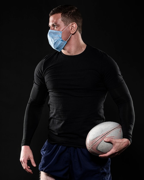 Giocatore di rugby maschile con maschera medica e palla