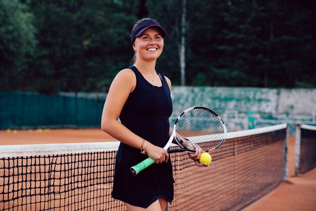 Giocatore di tennis. Attraente ragazza gioiosa, in piedi con la racchetta e pallina da tennis in campo