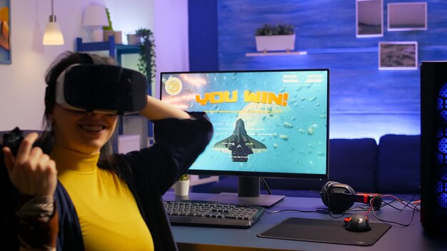 Giocatore donna che vince videogiochi sparatutto spaziale mentre indossa l'auricolare vr in studio di gioco