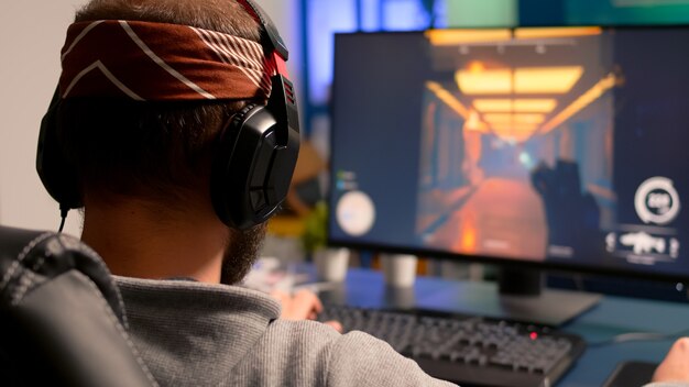 Giocatore professionista che gioca su un potente videogioco sparatutto in prima persona per computer durante il campionato dal vivo, indossando le cuffie. Torneo di videogiochi in streaming per giocatori competitivi utilizzando attrezzature professionali