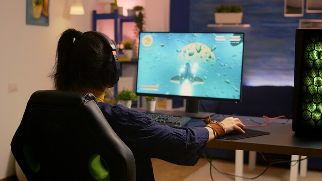 Giocatore vincitore seduto su una sedia da gioco alla scrivania e giocando ai videogiochi sparatutto spaziale con tastiera e mouse RGB