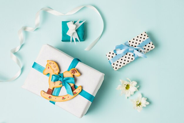 Giocattolo a dondolo con scatole regalo; fiori e nastro su sfondo blu
