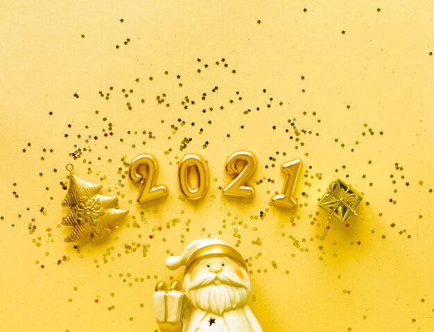 Giocattolo Babbo Natale con una confezione regalo in colore oro e la scritta 2021 su uno sfondo giallo Concetto di vacanza, vista dall'alto, copia dello spazio.