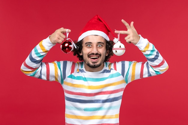 Giocattolo dell'albero di Natale della tenuta del giovane maschio di vista frontale sulla festa rossa del nuovo anno della parete rossa