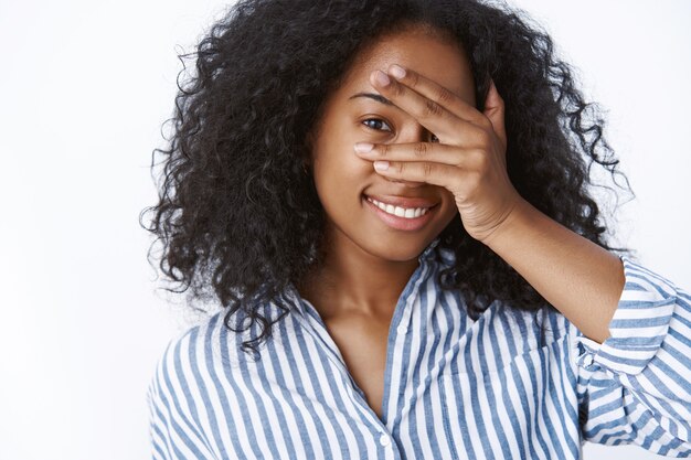 Giocosa affascinante ragazza adorabile che gioca a cucù esprimendo sensualità tenerezza tenendo i palmi del viso sbirciando attraverso le dita gioioso, sorridente denti ampiamente bianchi divertendosi spensierato