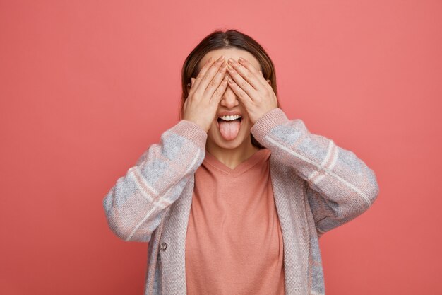 Giocosa giovane ragazza che copre gli occhi con le mani che mostrano la lingua