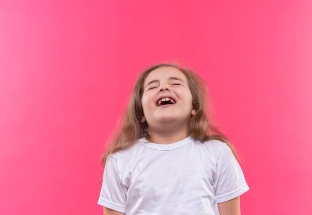 Gioiosa bambina della scuola che indossa la maglietta bianca sulla parete rosa isolata