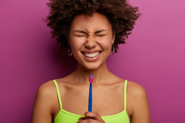 Gioiosa donna adulta dai capelli ricci sorride ampiamente, mostra denti perfetti e ben curati