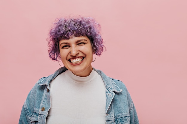 Gioiosa donna alla moda con piercing in bellissimi orecchini e in cima bianca e ride.