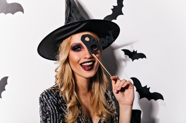 Gioiosa donna europea che propone allegramente in halloween. Adorabile giovane strega con trucco nero che esprime felicità.