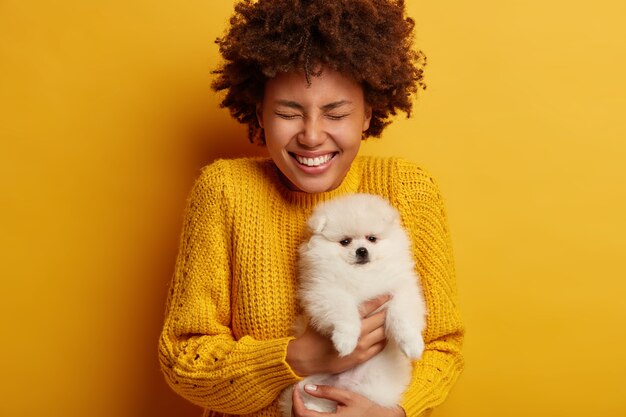 Gioiosa donna riccia con spitz bianco soffice porta il cane al salone di toelettatura, felice di ricevere l'animale domestico di razza preferito come regalo dal fidanzato