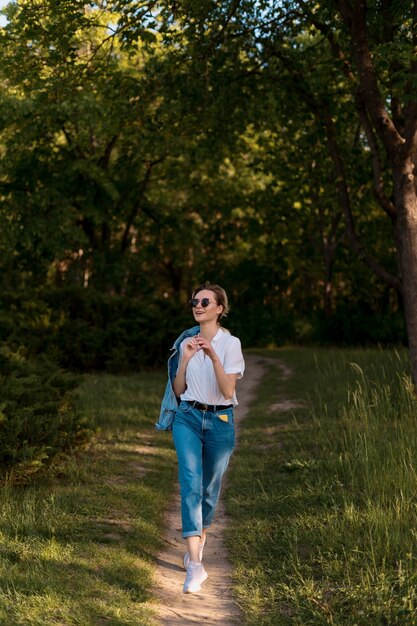 Gioiosa giovane donna con occhiali da sole alla moda che cammina nella natura in una bella giornata