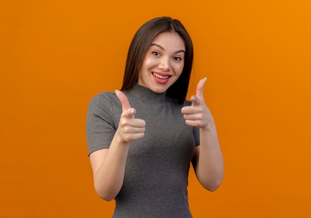 Gioiosa giovane donna graziosa che ti fa gesto in telecamera isolata su sfondo arancione con copia spazio