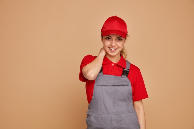 Gioiosa giovane operaio edile femminile che indossa l'uniforme e cappuccio tenendo la mano sul collo