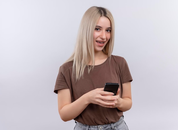 Gioiosa giovane ragazza bionda in parentesi graffe dentali tenendo il telefono cellulare su uno spazio bianco isolato con copia spazio