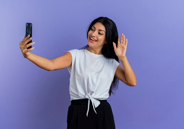 Gioiosa giovane ragazza caucasica alza la mano tenendo e guardando il telefono