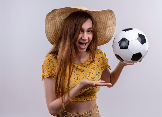 Gioiosa giovane ragazza che indossa il cappello tenendo il pallone da calcio su uno spazio bianco isolato