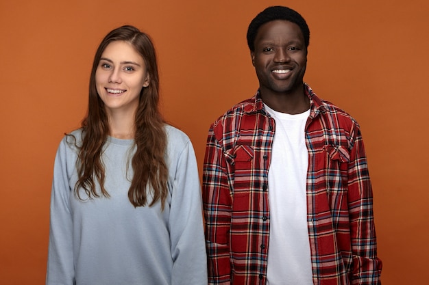 Gioioso attraente giovane afroamericano in camicia a quadri sorridendo felicemente, mostrando i suoi denti bianchi perfetti mentre trascorre molto tempo con la sua ragazza caucasica, con sguardi felicissimi