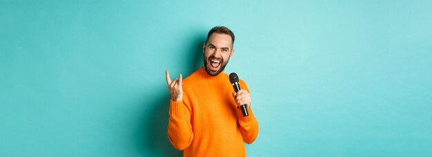 Gioioso bell'uomo che canta una canzone nel microfono che mostra un gesto rocknroll eccitato in piedi sopra il turqu