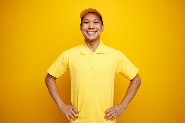 Gioioso giovane fattorino che indossa cappello e uniforme mantenendo le mani sulla vita