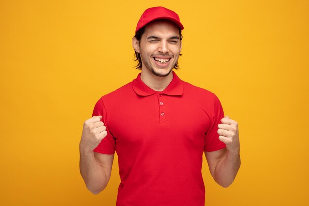 gioioso giovane fattorino che indossa uniforme e cappuccio che mostra sì gesto con gli occhi chiusi isolato su sfondo giallo