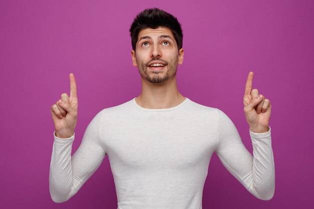 Gioioso giovane uomo bello che punta e alza lo sguardo su sfondo viola