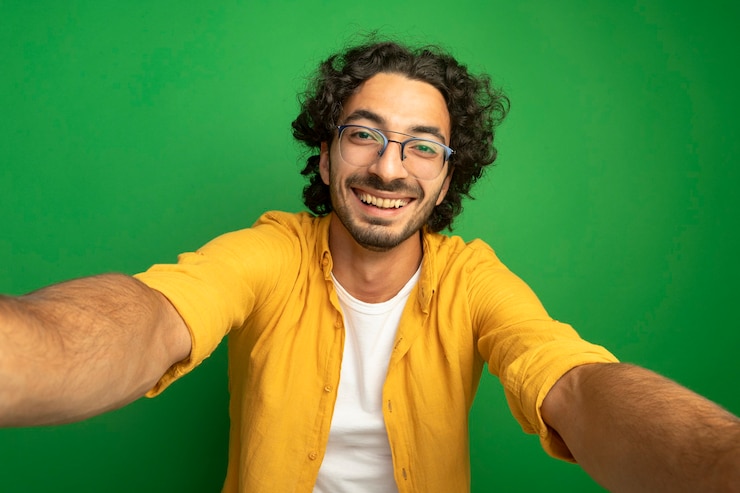 Foto gratuito gioioso giovane uomo caucasico bello con gli occhiali che guarda l'obbiettivo allungando le mani verso la telecamera isolata su sfondo verde