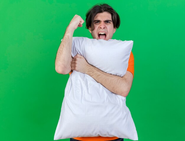 Gioioso giovane uomo malato abbracciò il cuscino mostrando sì gesto isolato su sfondo verde