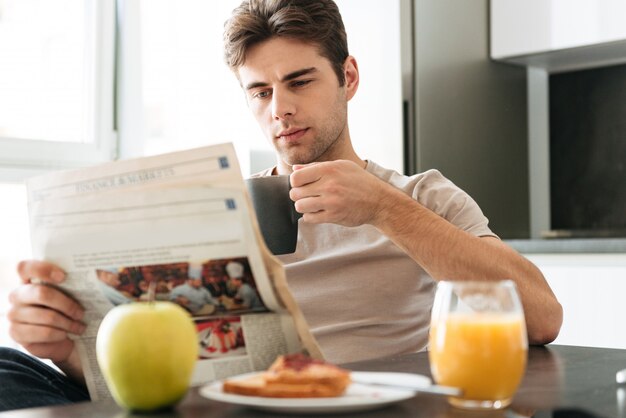 Giornale della lettura dell'uomo concentrato giovani mentre sedendosi nella cucina