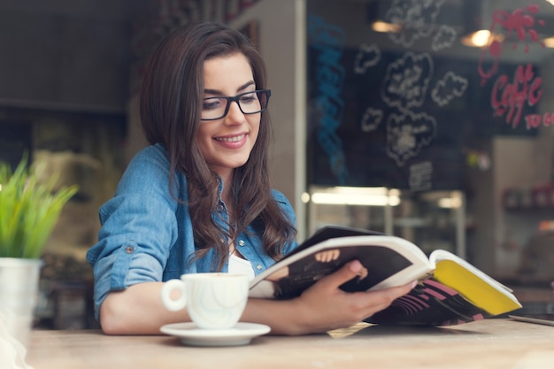 Giornale sorridente della lettura della donna al caffè