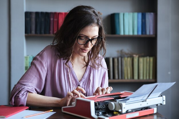 Giornalista maturo castana della donna in occhiali che scrive sulla macchina da scrivere all'interno