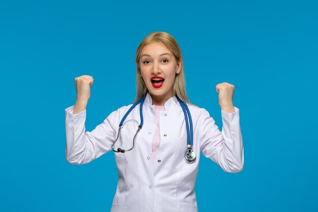 Giornata mondiale dei medici eccitato giovane dottore biondo con i pugni sullo stetoscopio nel camice