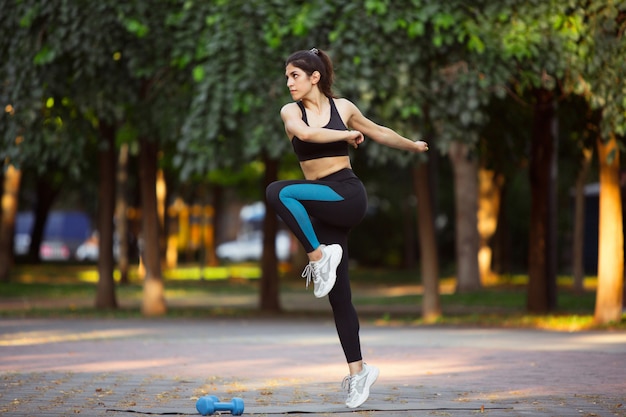 Giovane addestramento dell'atleta femminile nella via della città nel sole di estate. Bella donna che pratica, che lavora. Concetto di sport, stile di vita sano, movimento, attività. Stretching, sit-up, ABS.