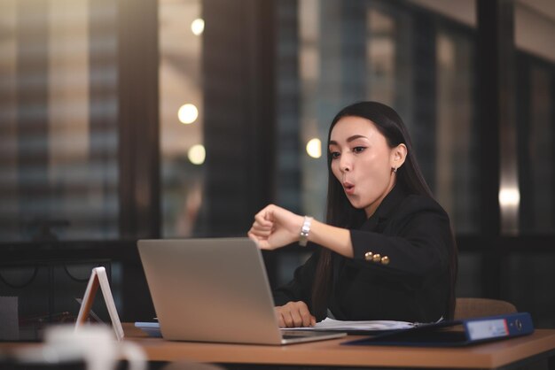 Giovane adulto asiatico intelligente donna d'affari in abito nero casual utilizzando laptop che fa gli straordinari in ufficio urbano